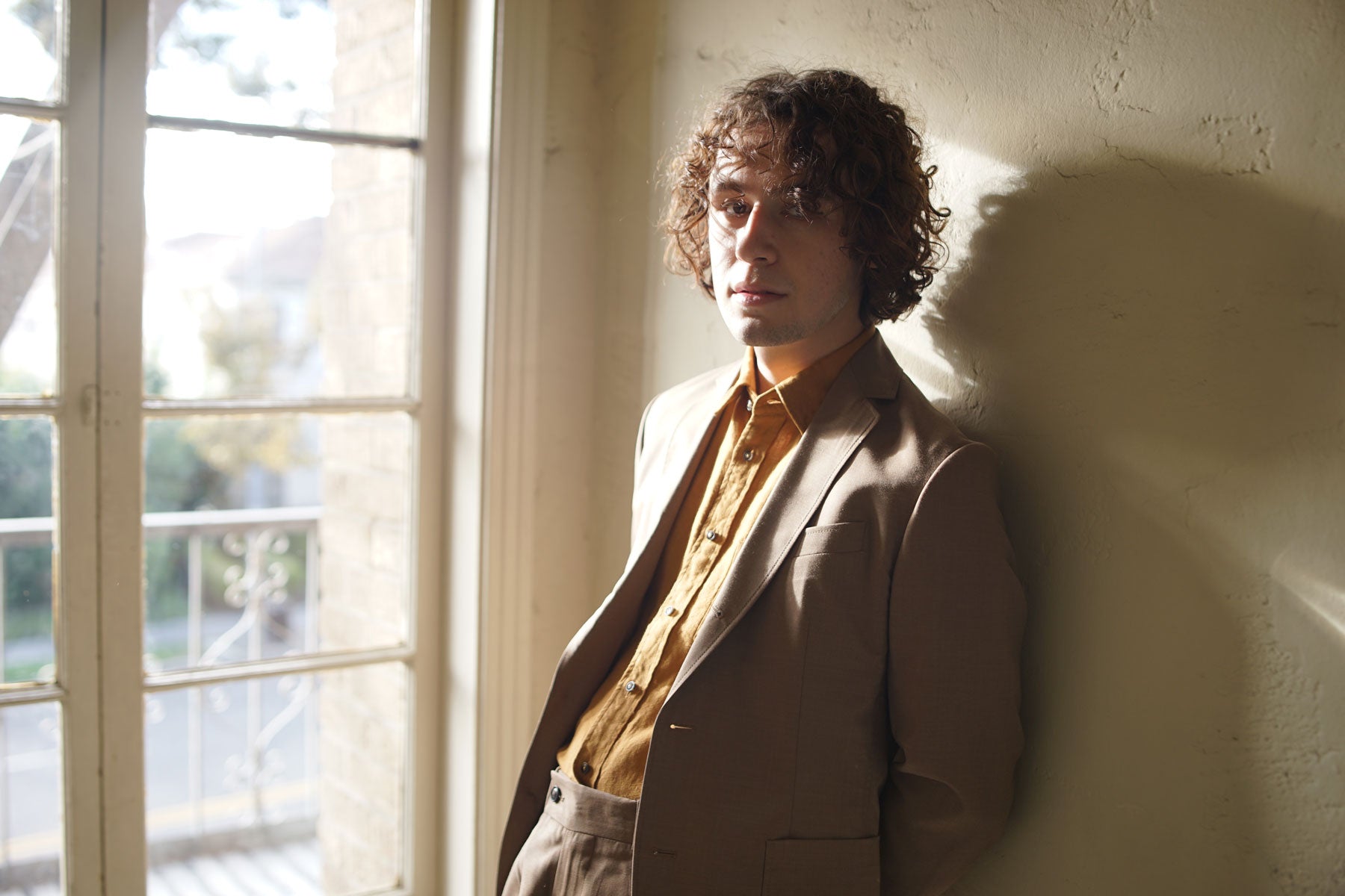 Model wears tan suit and gold button down shirt.