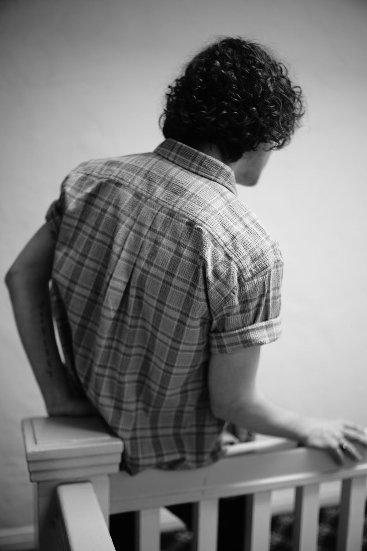 Close-up from the back of model wearing plaid short sleeve shirt. Photo is black and white.