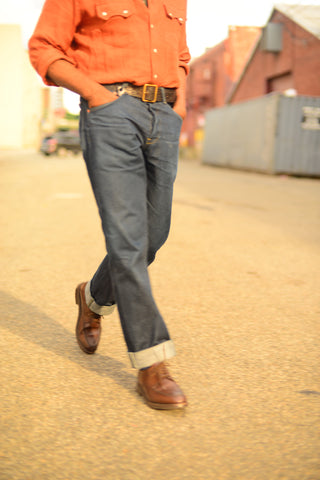 Close-up image of Glenn wearing cuffed jeans, brown dress shoes, and an orange western shirt tucked in with a brown leather belt.