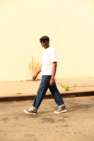 Image of Glenn walking down a street wearing jeans, a white t-shirt, and sneakers.
