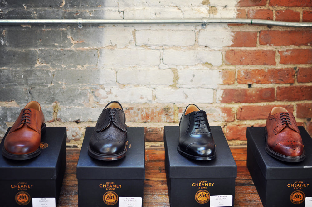 Image of four pairs of Cheaney dress shoes sitting on top of their respective shoe boxes. They are shot in front of a brick wall.