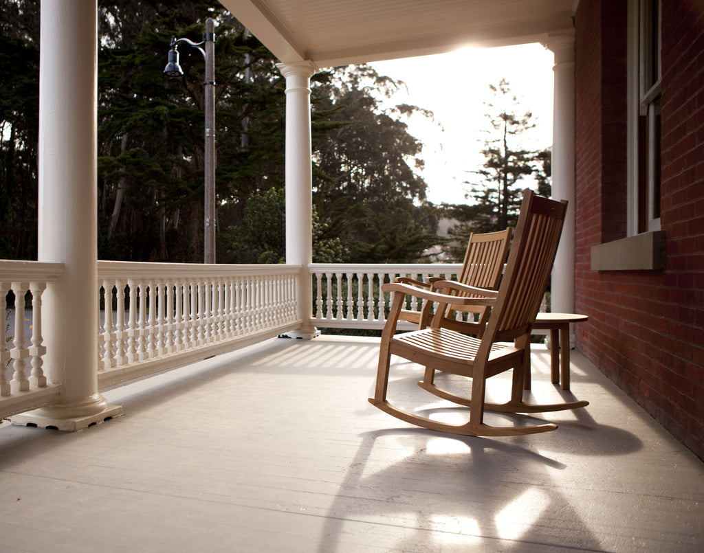 Two rocking chairs sit on the porch of the Inn at Presidio as the sun sets behind the trees. 