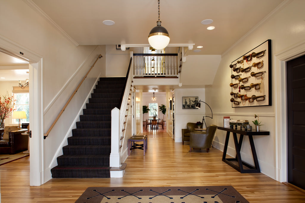 A well decorated foyer at the Inn at Presidio. We are at the bottom of a carpeted staircase, on a hardwood floor. Elegant furniture and stylish art installations decorate the open space. 