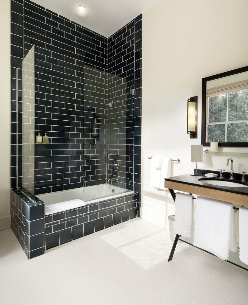 A white tile bathroom that features a glossy black tile shower, bathtub, and a stylish sink with a black countertop.