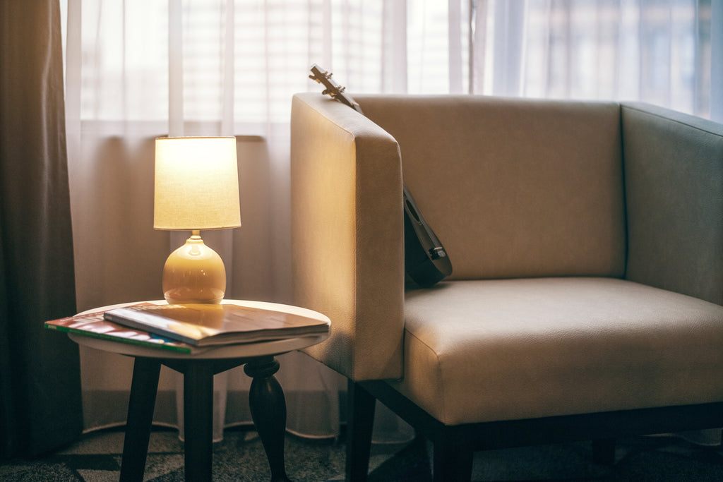 A small black ukulele rests on a modern style chair with leather upholstery. 