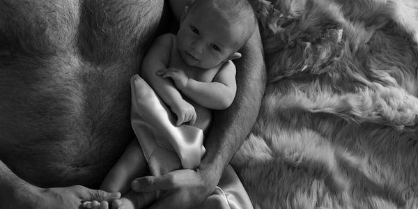 black and white photo of man in bed with baby with luxury blankets by JG Switzer