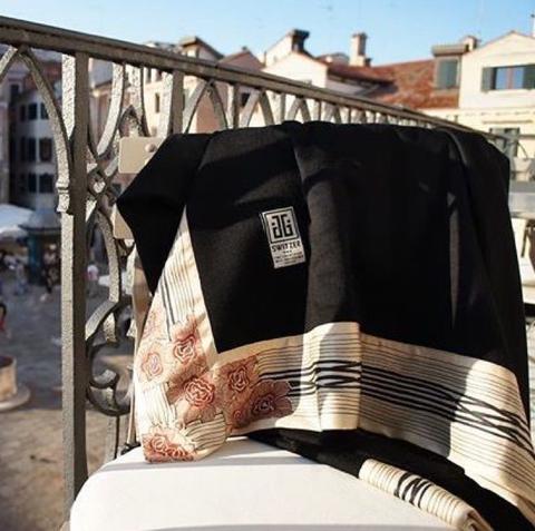 Now Voyager luxury travel blanket in black hanging in the balcony in Venice with it's golden silk borders beaming in the sunlight.