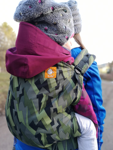 A mother carrying her child in back-carry position while in the nature.