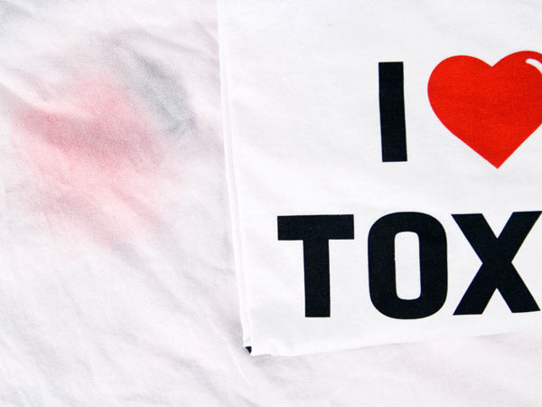 close up view of two i heart toxic waste shirts, one is shown with ink bleeding through the back of shirt and one is new and crisp