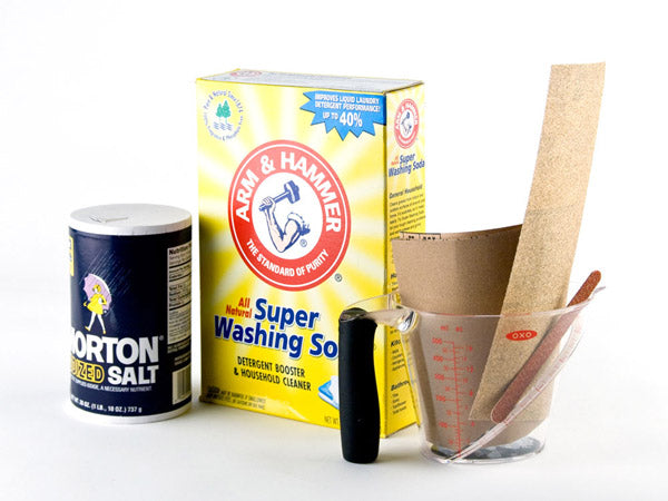 container of salt, container of super washing soda, a variety of sandpaper samples, and a clear plastic mixing cup