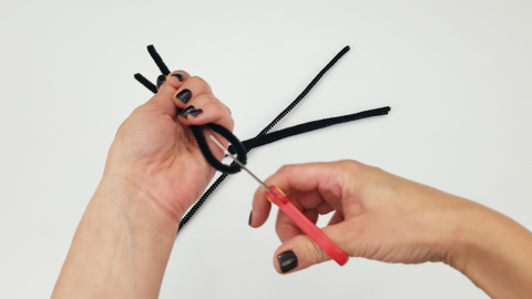 Scissors cutting four chenille stems in half