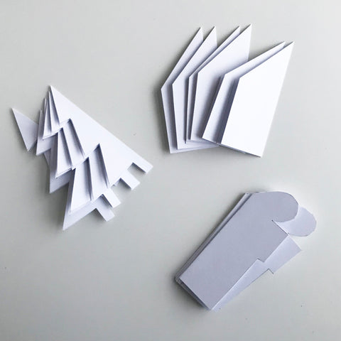 Paper cut in the shape of a tree, house, and Christmas present