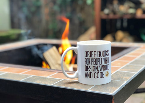 A Book Apart mug in front of an outdoor fire pit.