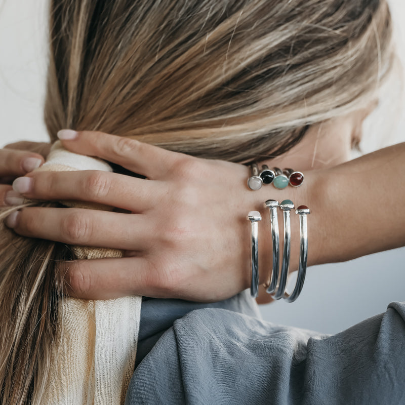 Blond female holding her ponytail. On her right wrist, she is wearing three, silver, semi precious stone bracelets by 3rd Floor