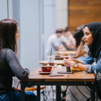 2 ladies sat at a table with coffees talking