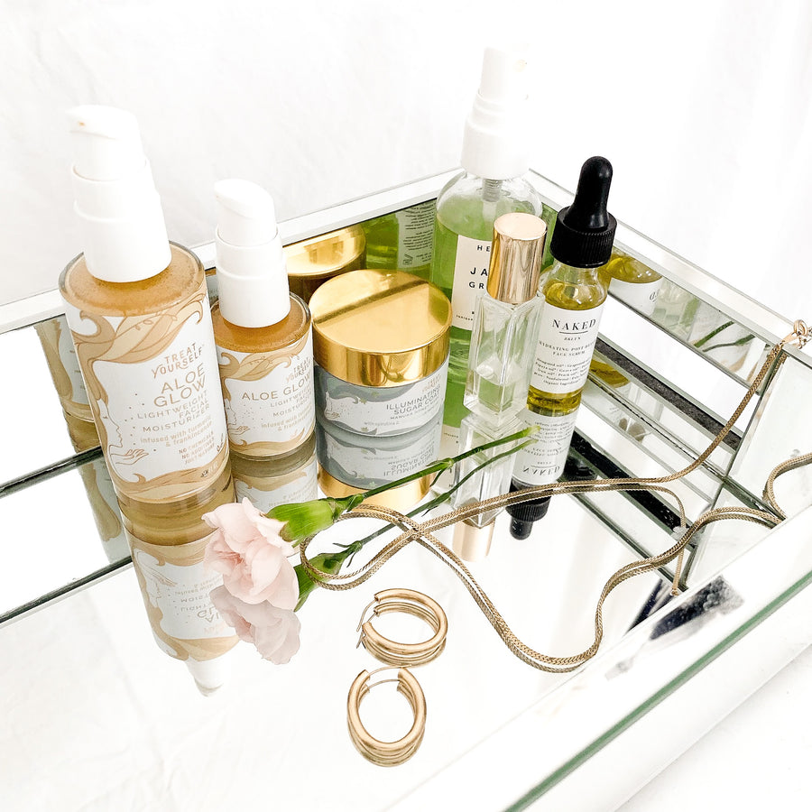 Mirror tray holding Aloe Glow bottles, Illuminating Sugar Coat, gold jewelry, small flower and other perfumes and serums