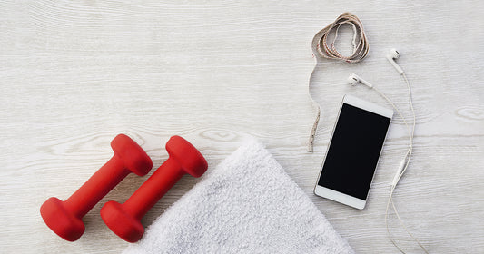 red dumbbells, white towel, mobile phone, headphones, measuring tape on white wooden surface