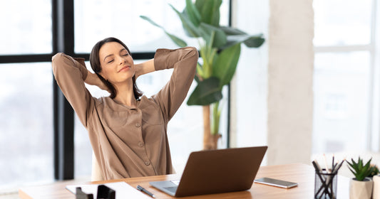 a woman sitting at desk leaning back with eyes closed and hand on the back of her head