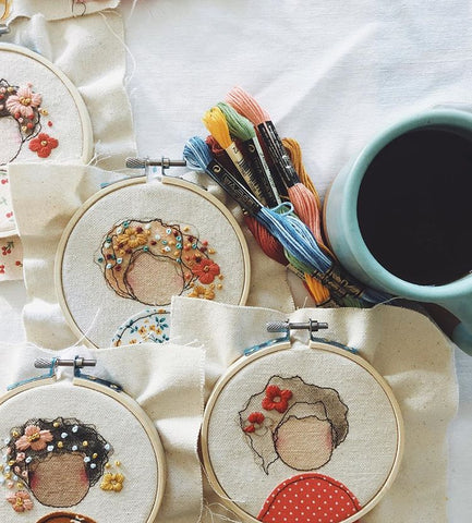 Unfinished embroidery hoops on a table next to embroidery floss and a cup of coffee