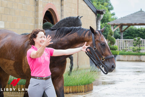 Woman stood next to horse with arms extended ready to greet someone with a hug