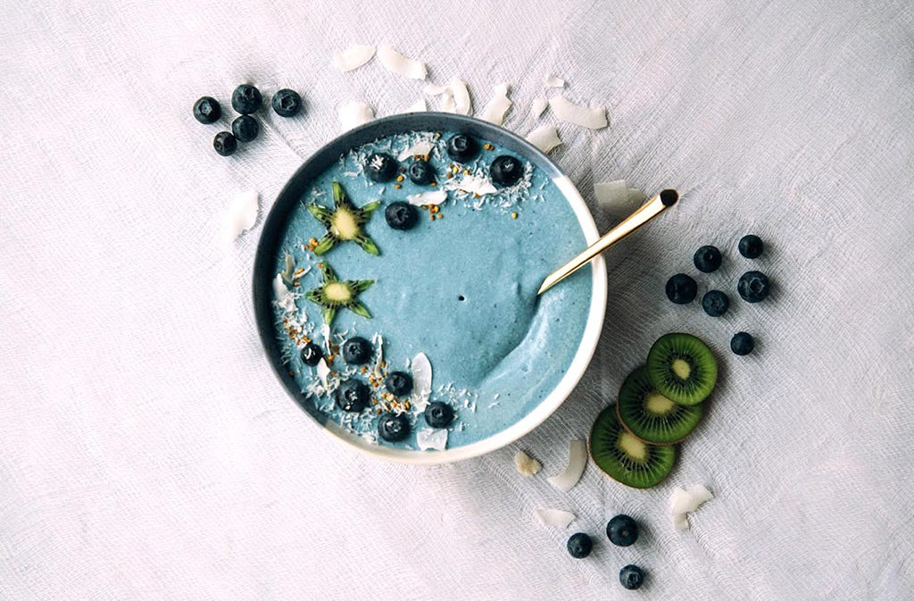 blue keto smoothie bowl topped with blueberries kiwi and coconut flakes