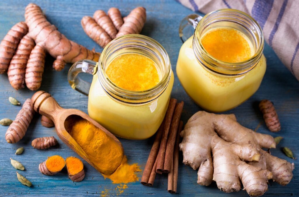 two mugs of turmeric bone broth protein shake surrounded by ginger and turmeric powder