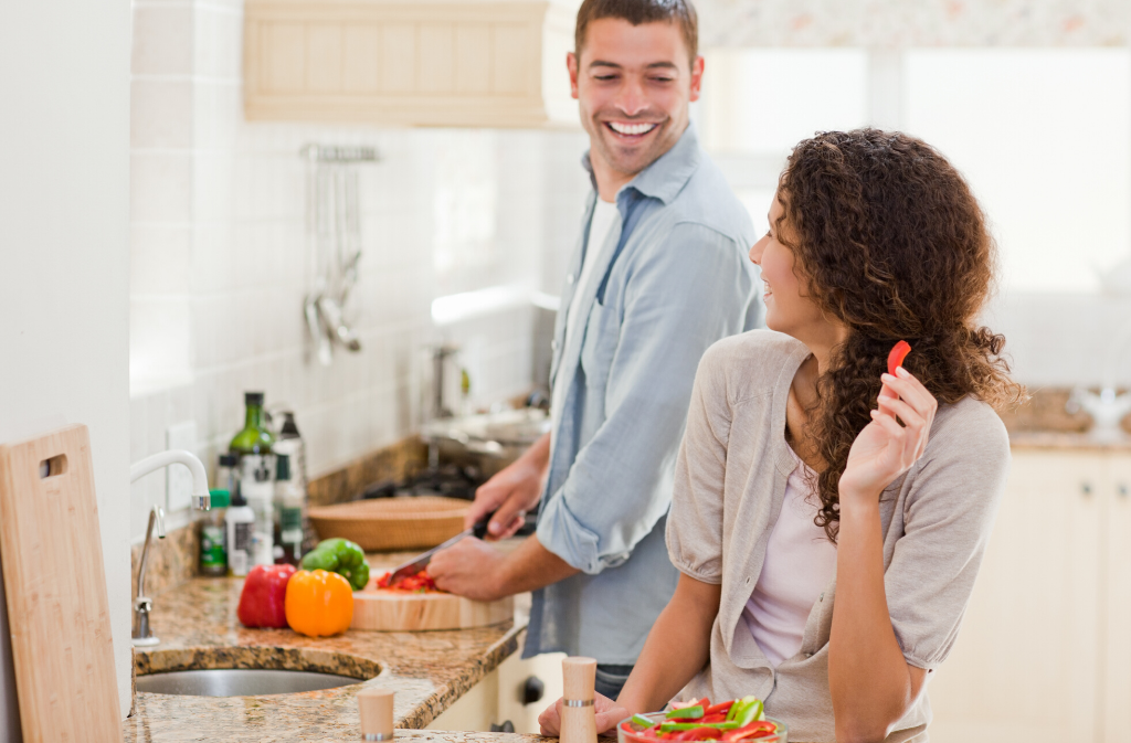 man chopping vegetables in kitchen while smiling at woman who is looking back at him