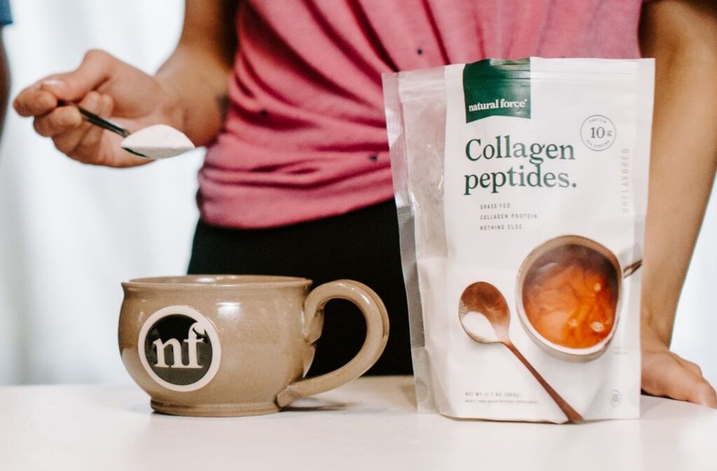 woman adding a spoonful of collagen peptides to a handcrafted natural force mug beside a bag of natural force collagen peptides
