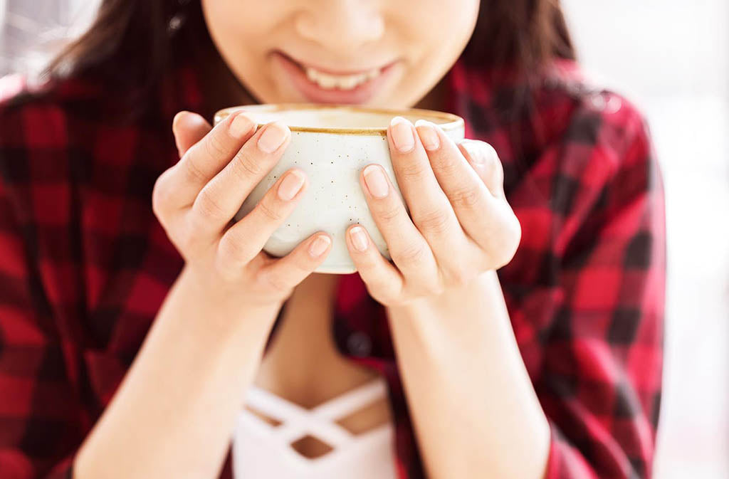 woman in flannel smiling and lifting a mug up to her hands