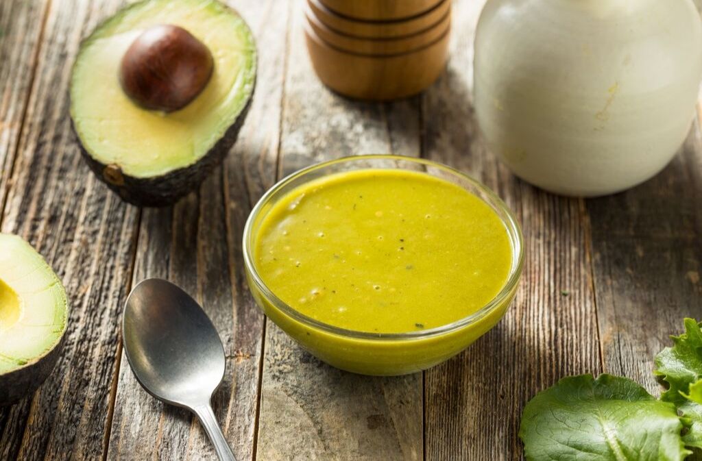 a bowl of keto green goddess salad dressing beside a spoon and an avocado