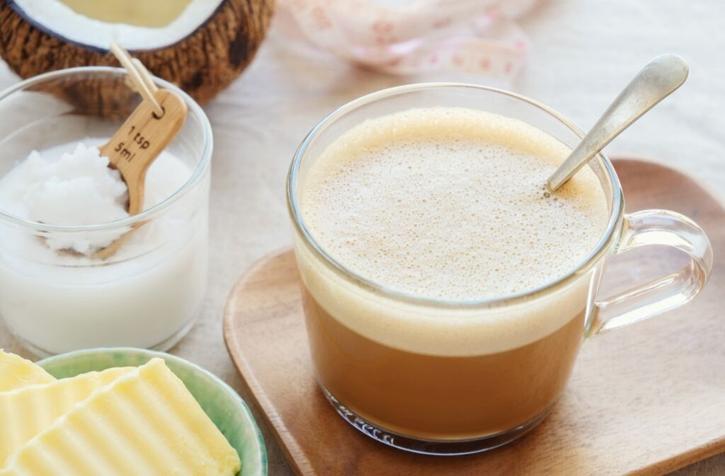 clear mug of dairy free keto bullet coffee on a tray surrounded by butter coconut oil and a coconut