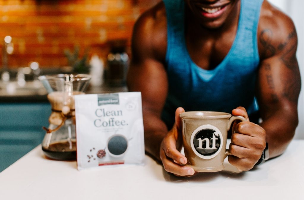 athletic man holding out a handmade natural force mug of dairy free keto coffee beside a bag of natural force clean coffee