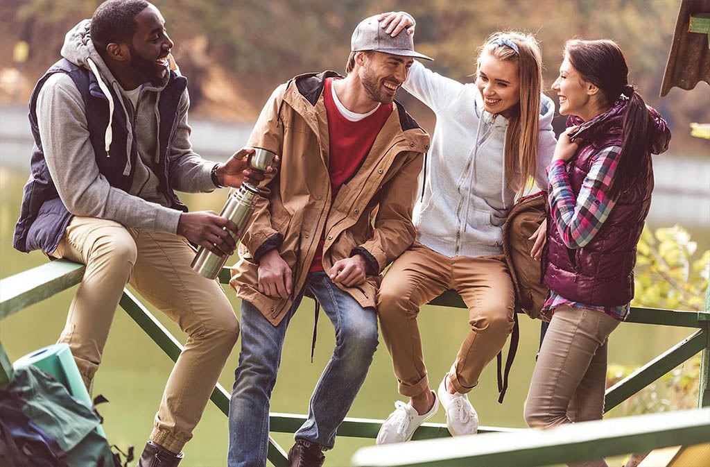 group young adults sitting on a fence smiling and laughing