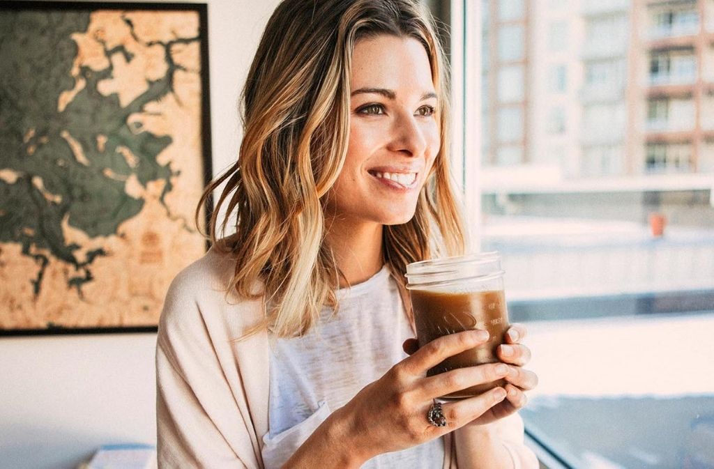 blonde woman smiling and holding a mason jar of iced keto americano