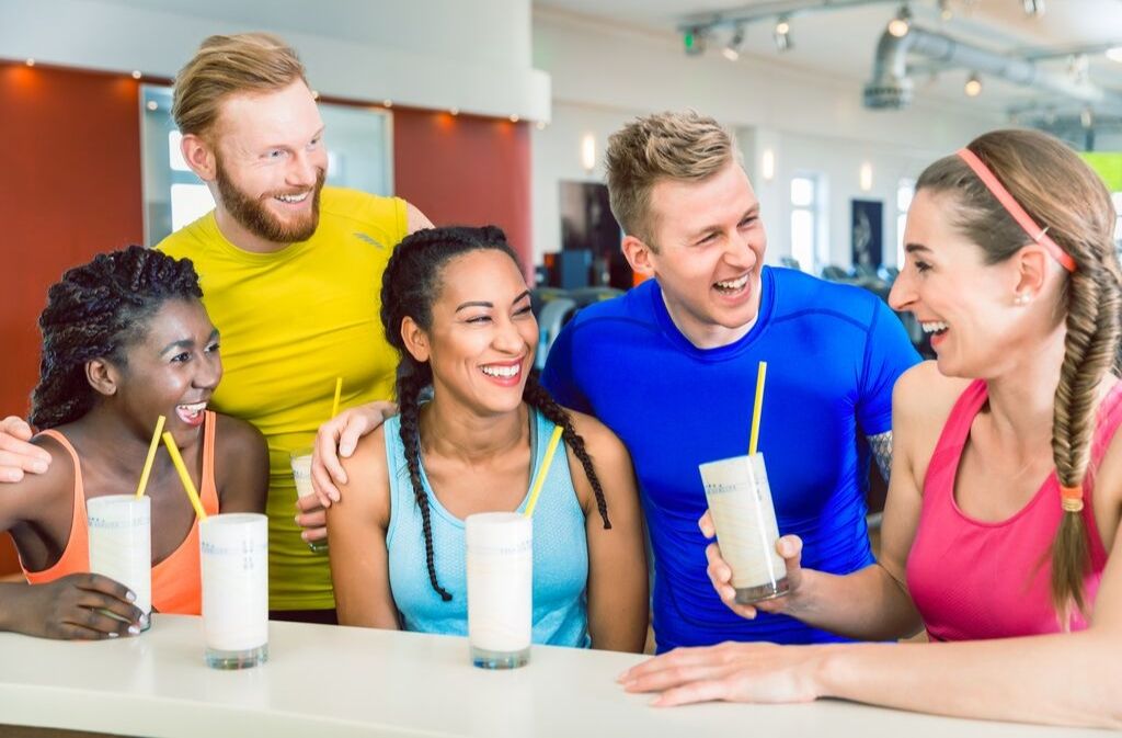 five athletes smiling and laughing while drinking silky smooth protein shakes 