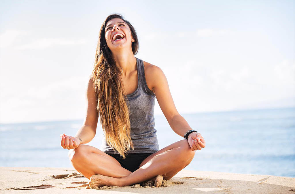 woman in meditation position on a beach laughing