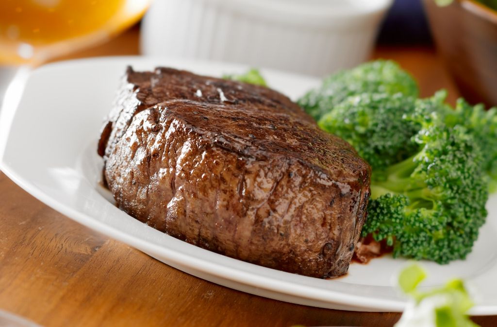 a white plate with sirloin steak beside broccoli