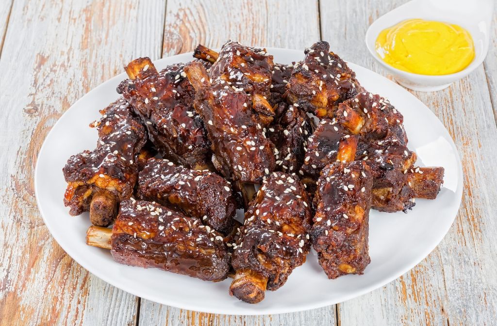 a plate of keto friendly chinese spare ribs with a small bowl of yellow sauce