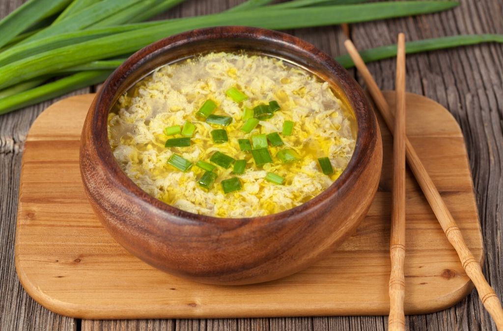 a wooden bowl of keto friendly egg drop soup beside chopsticks