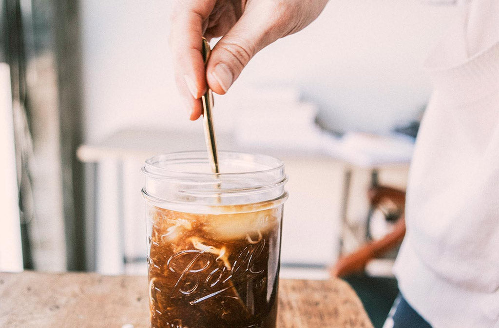 hand stirring a glass of keto americano and keto coffee creamer