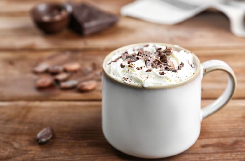 a ceramic mug of keto hot chocolate topped with whipped cream and chocolate shavings on a wood surface