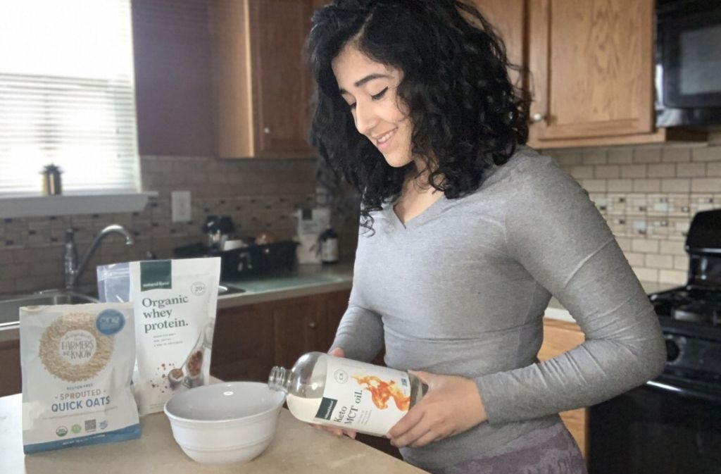 angie hernandez in a kitchen smiling while pouring natural force keto mct oil into a bowl