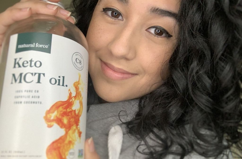 close up of angie hernandez looking at the camera and smiling while holding out a bottle of natural force keto mct oil