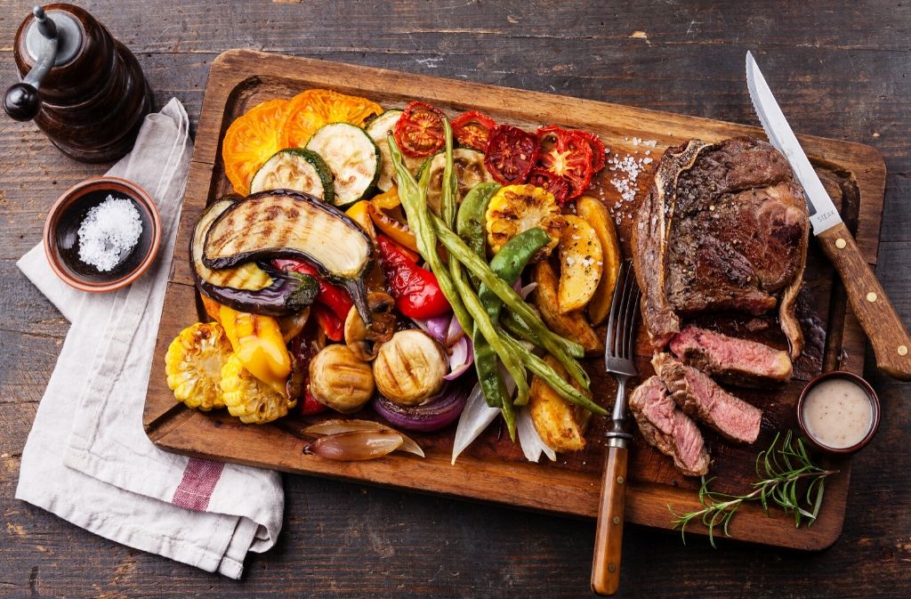 cutting board with sliced sirloin steak and mixed grilled vegetables