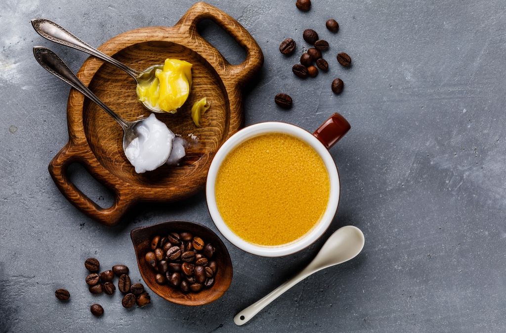 an overhead view of a mug of keto rocket fuel latte surrounded by coffee beans a spoon of butter and a spoon of coconut oil