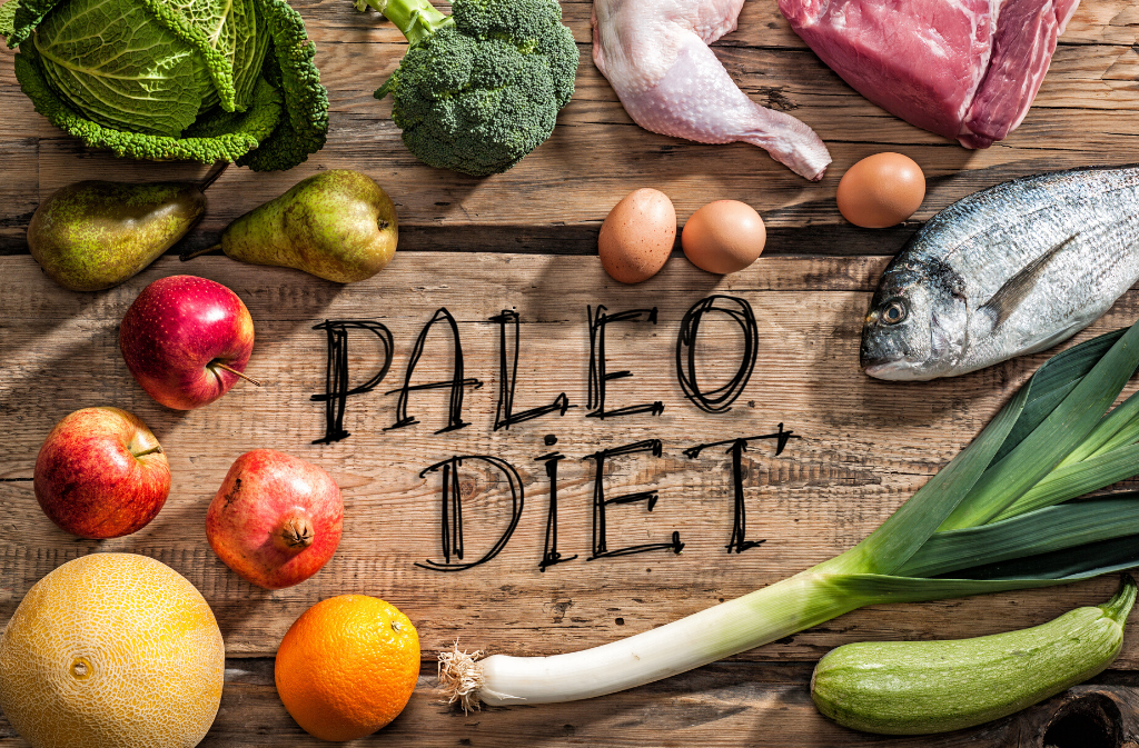 a spread of paleo diet foods like leek apple and eggs on a wooden surface with the text paleo diet in the middle