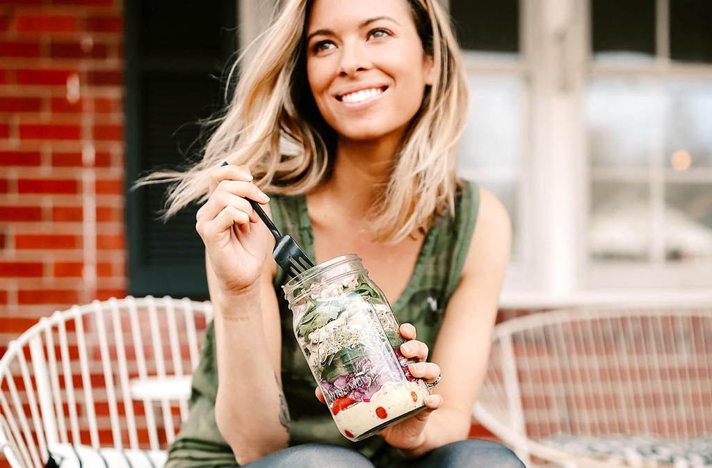 woman smiling eating a mason jar salad
