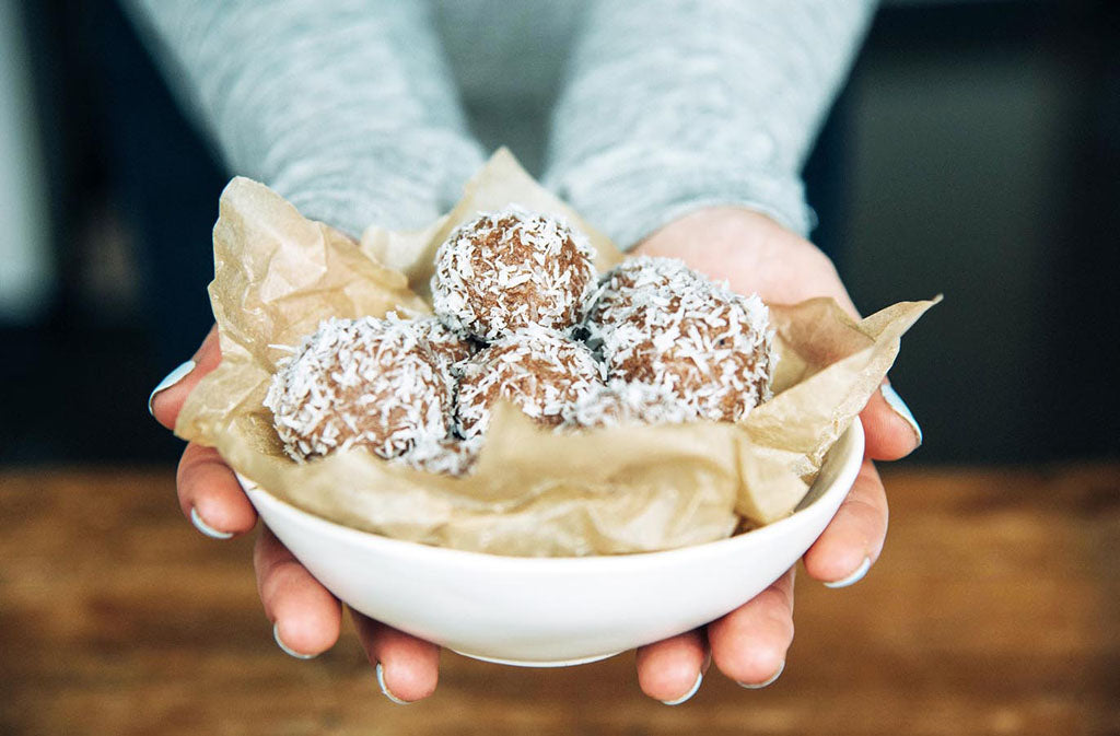 woman's hands holding out a white bowl filled with keto energy bites