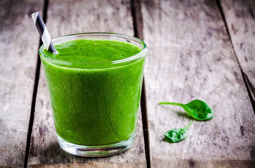 a glass of healthy green breakfast smoothie on a wood surface  beside two spinach leaves
