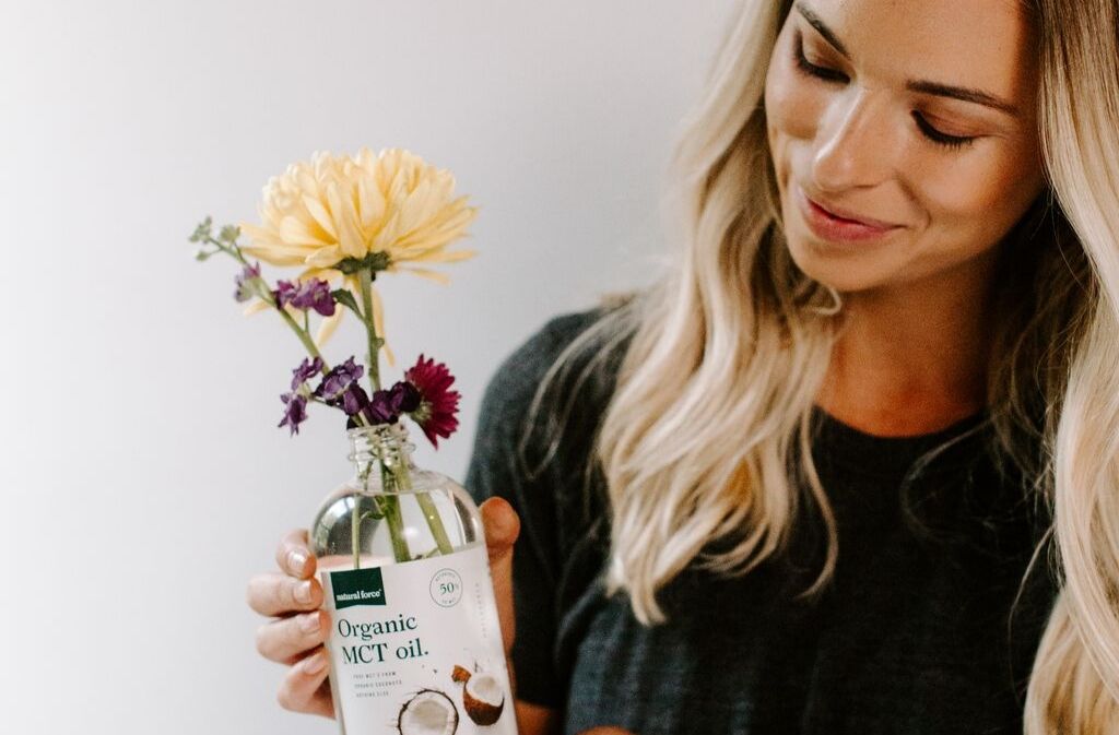 fit woman smiling at a bottle of natural force organic mct oil containing flowers